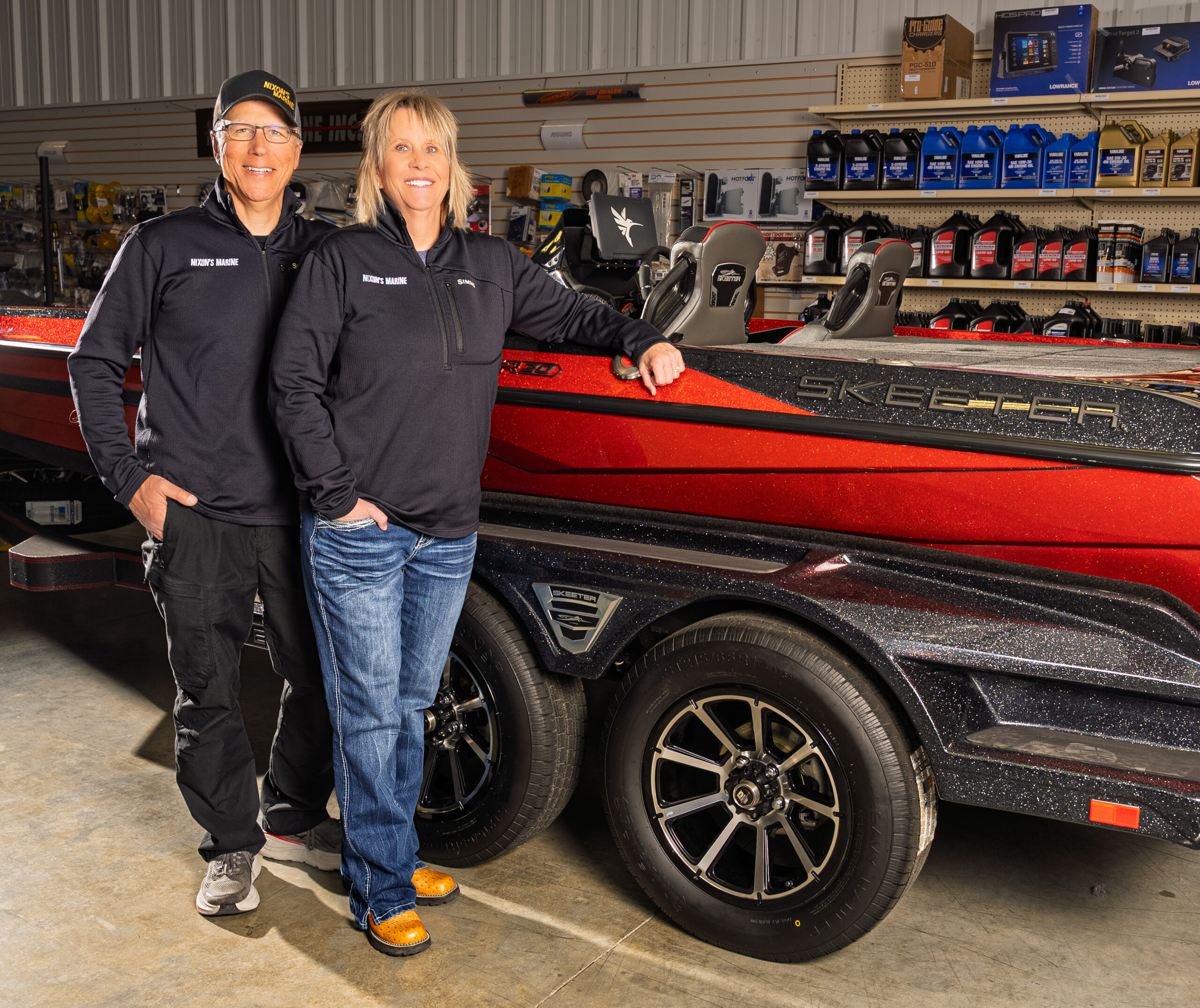 Two people posing with a red fishing boat